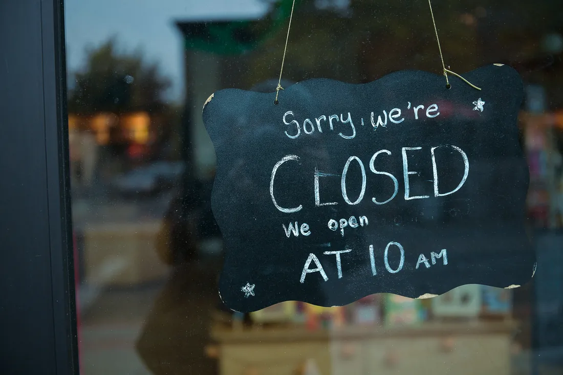 A chalkboard hanging inside a shop window, hand-lettered: sorry, we&rsquo;re closed, we open at 10 am.