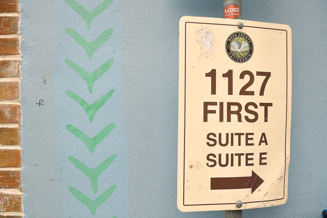 A street sign in downtown Napa under the Napa County seal: 1127 First, Suite A, Suite E, with an arrow pointing right.